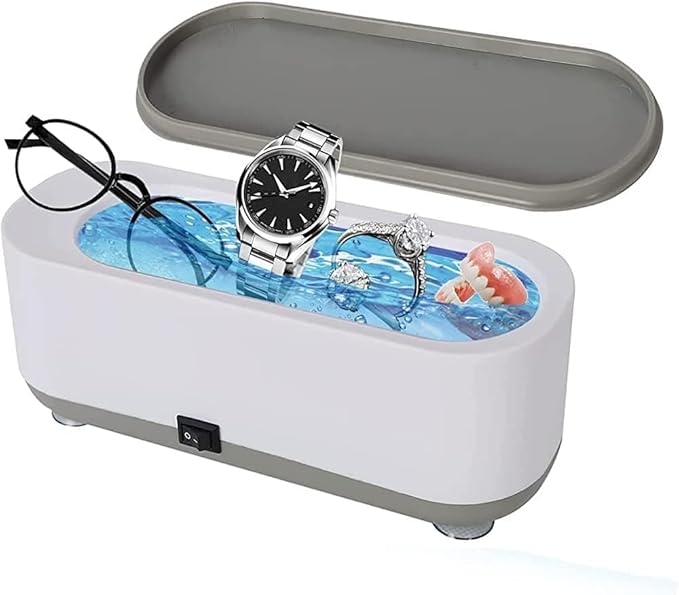 White compact jewellery cleaner with its grey lid open; eyeglasses, ring and watch pictured around the basin